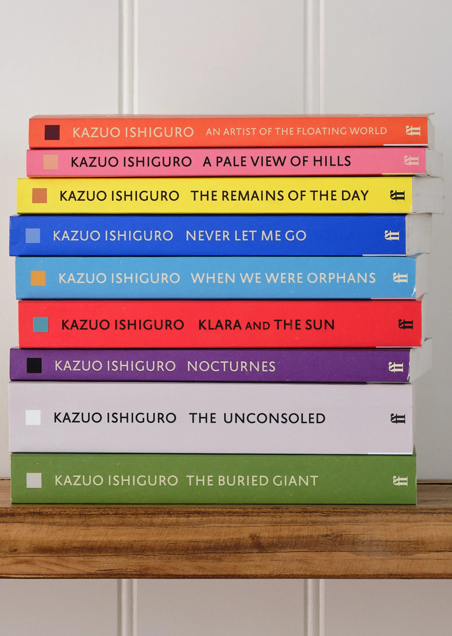 Nine Kazuo Ishiguro titles stacked spine-out in Faber's rejacketed uniform edition designed by Pete Adlington — An Artist of the Floating World, A Pale View of Hills, The Remains of the Day, Never Let Me Go, When We Were Orphans, Klara and the Sun, Nocturnes, The Unconsoled and The Buried Giant, each on a different ground with the same square device